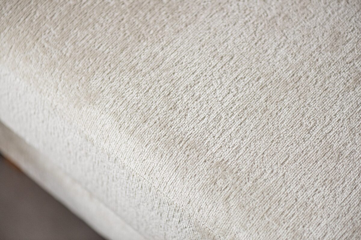 Close-up van een lichtbeige textuurstof met een subtiel geweven patroon. Het materiaal lijkt glad met een lichte glans, waardoor de ingewikkelde details van het weefsel worden benadrukt.