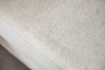 Close-up van een lichtbeige textuurstof met een subtiel geweven patroon. Het materiaal lijkt glad met een lichte glans, waardoor de ingewikkelde details van het weefsel worden benadrukt.