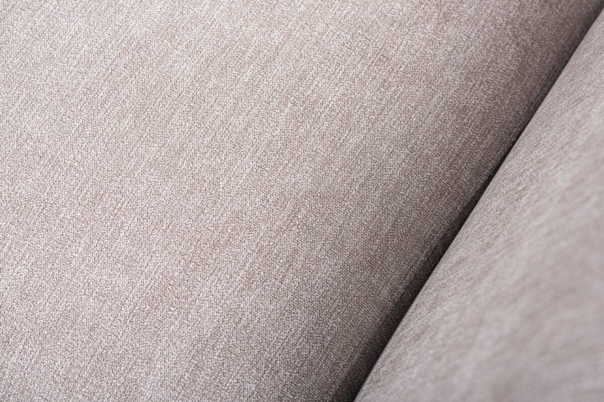 Close-up van een beige stoffentextuur met een subtiel geweven patroon. De afbeelding legt de details en het gladde uiterlijk van de stof vast, en toont de neutrale kleur en zachte textuur.