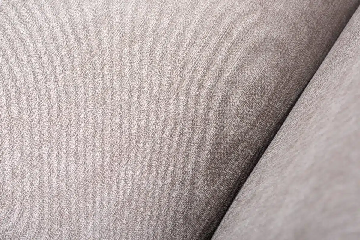 Close-up van een beige stoffentextuur met een subtiel geweven patroon. De afbeelding legt de details en het gladde uiterlijk van de stof vast, en toont de neutrale kleur en zachte textuur.