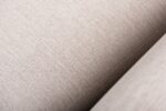Close-up van beige textuurstof, met gedetailleerde weefstructuur en nerf. Het patroon is subtiel en uniform, wat de zachtheid en neutrale toon van de stof benadrukt.