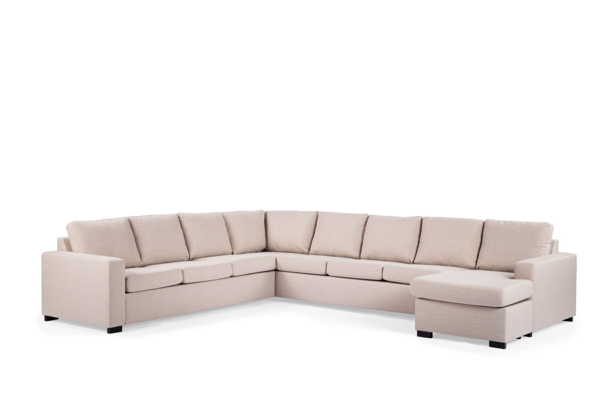 Een beige L-vormige sectionele bank met gestoffeerde zittingen en rugleuningen. De bank heeft een chaise longue-gedeelte aan de rechterkant en wordt ondersteund door korte zwarte poten, tegen een witte achtergrond.