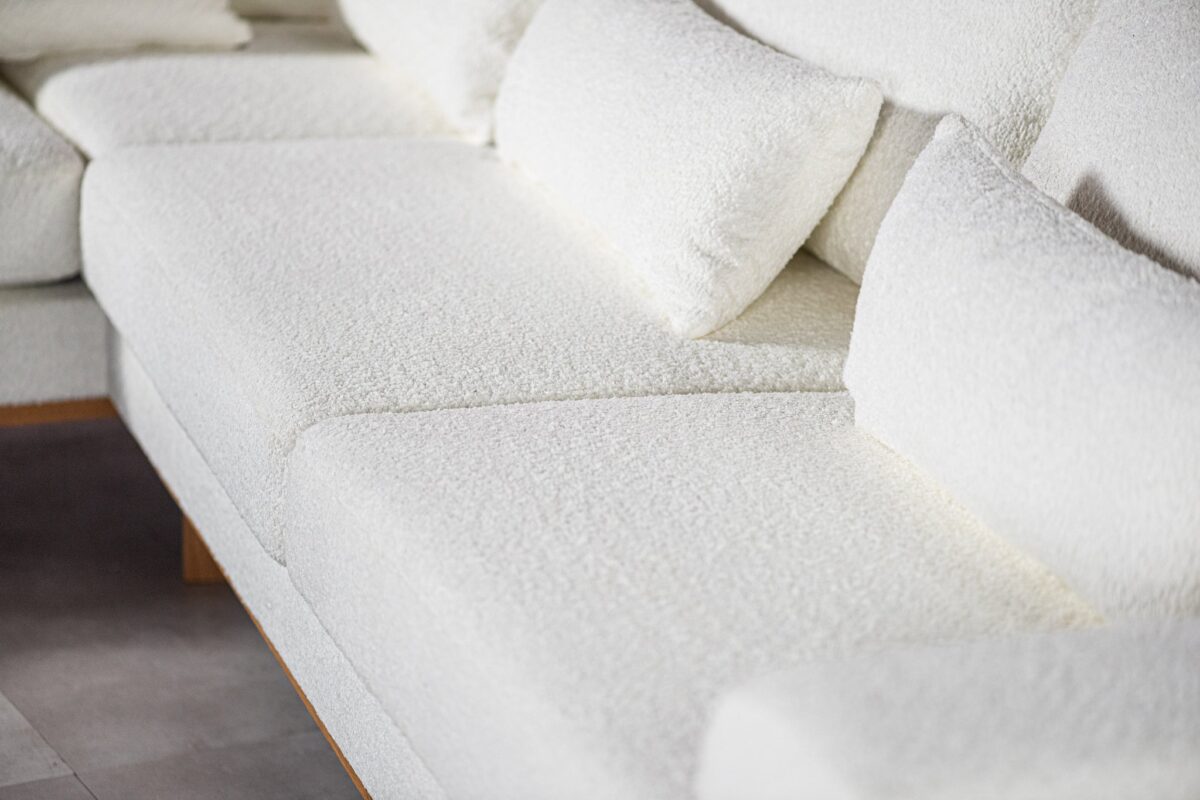 Close-up van een moderne, witte, getextureerde sectionele bank met pluche kussens. De stof heeft een zachte, donzige uitstraling. De bank staat op een gladde, lichtgekleurde vloer en de afbeelding richt zich op de textuur en het ontwerp van het zitgedeelte.