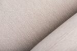 Close-up van een lichtbeige stof met een subtiele, geweven textuur. Het oppervlak toont fijne draden die horizontaal en verticaal lopen, waardoor een eenvoudig maar elegant patroon ontstaat.