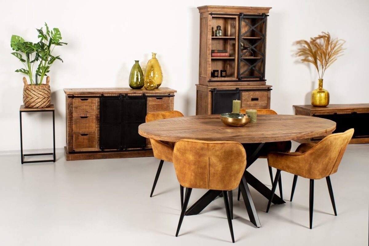 Eetkamer met een ronde houten tafel en vier bruine stoelen. Een houten kast, dressoir en plant sieren de ruimte. Twee gele vazen en kaarsen voegen kleur toe. De vloer is lichtgekleurd en de muren zijn effen, wat een gezellige, moderne sfeer versterkt.