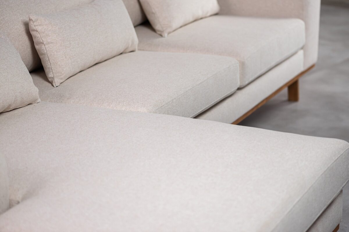 Close-up van een beige sectionele bank met pluche kussens. De stof lijkt zacht en getextureerd. De bank staat op een lichtgekleurde vloer, wat een moderne en minimalistische interieursetting suggereert.