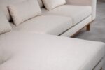 Close-up van een beige sectionele bank met pluche kussens. De stof lijkt zacht en getextureerd. De bank staat op een lichtgekleurde vloer, wat een moderne en minimalistische interieursetting suggereert.