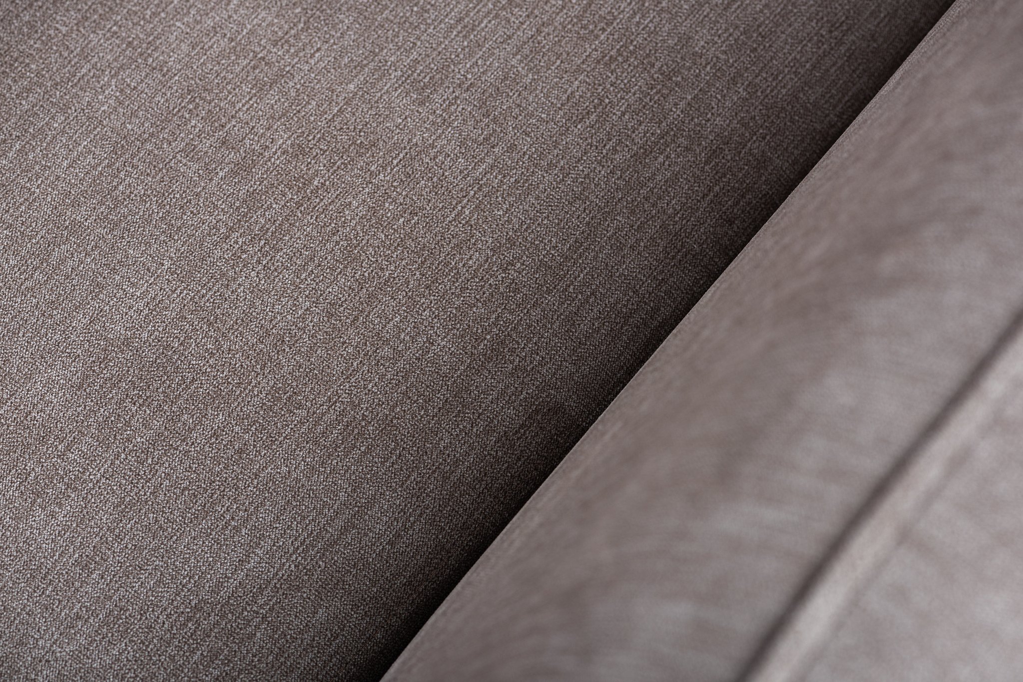 Close-up van een getextureerd, lichtbruin stoffen oppervlak met subtiele diagonale patronen. De afbeelding legt het ingewikkelde weefsel en de fijne details van het materiaal vast.