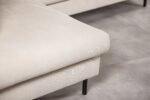 Close-up van een beige gestoffeerde bank met structuurstof, met metalen poten op een lichtgrijze betegelde vloer. De focus ligt op de armleuning en de zithoek van de bank.