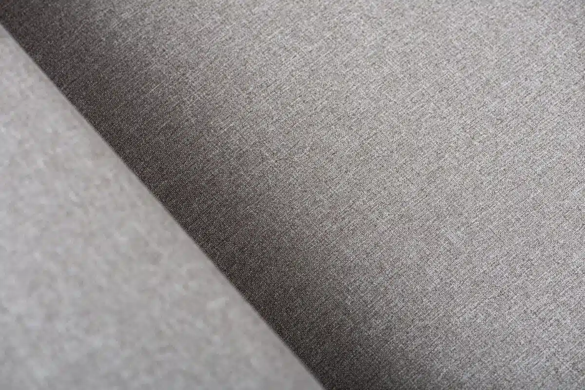 Close-up van een grijze stof met textuur, diagonale lijnen en zachte belichting. De weefstructuur en fijne details van de stof zijn goed te zien.