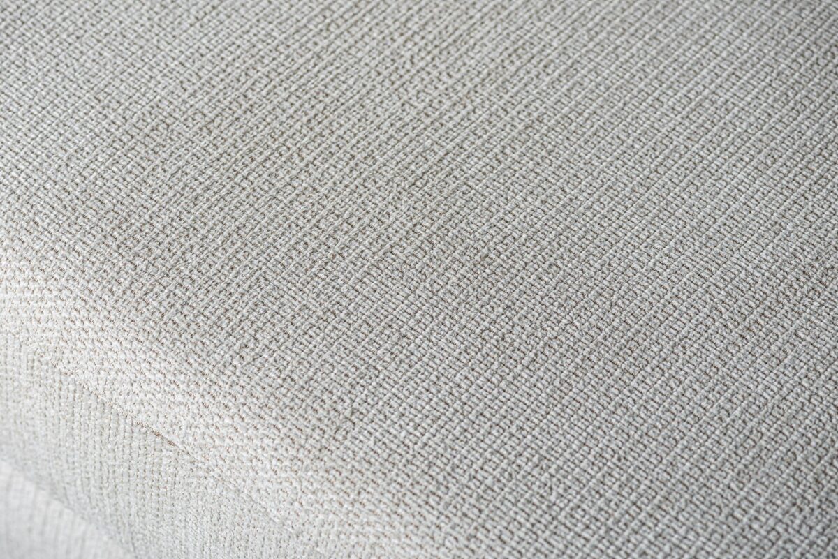 Close-up van de gestructureerde, geweven Lord 22 stof in beige (E460) op de 3 zits hoek links sofa, die de bekleding en het kussenoppervlak laat zien.