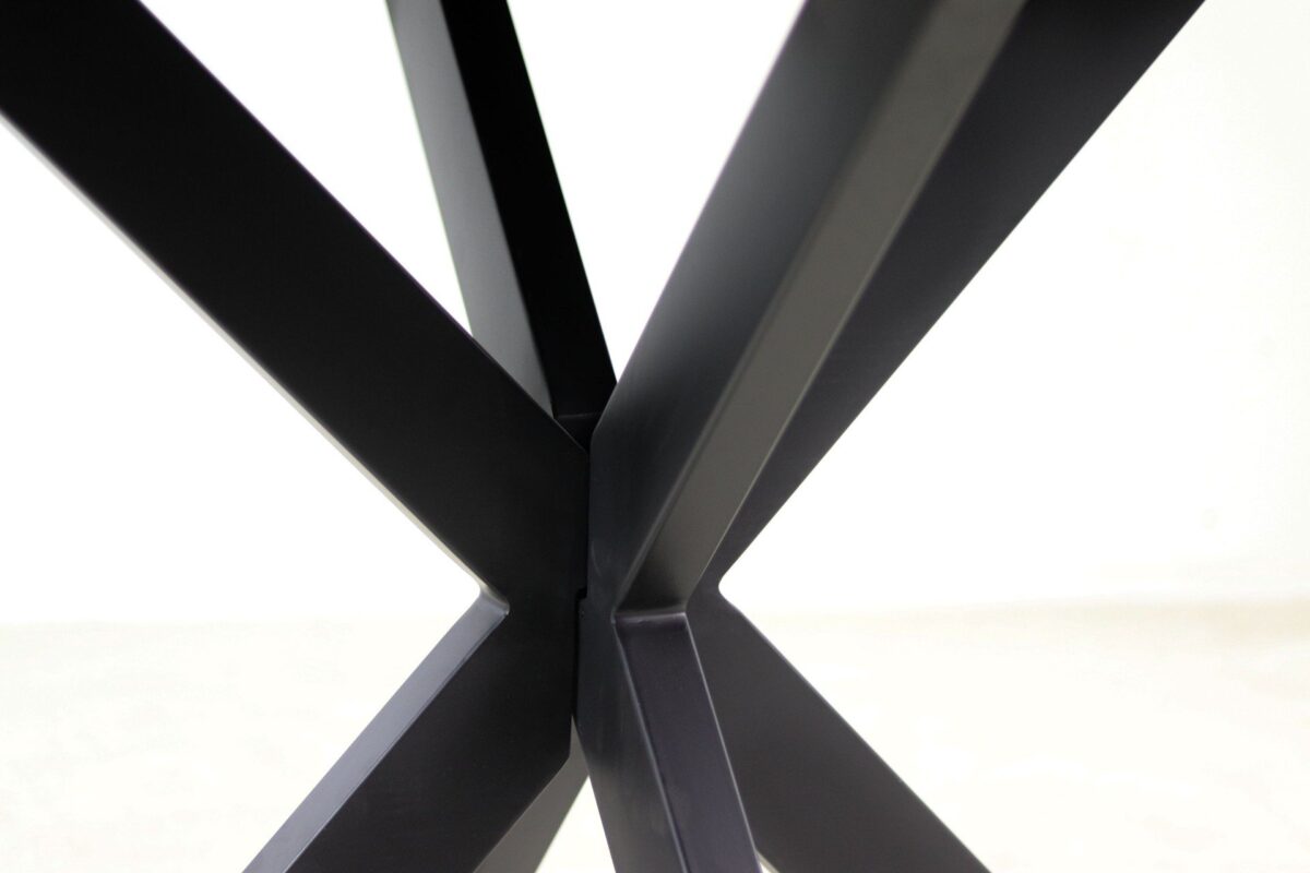Close-up van kruisende zwarte metalen tafelpoten die een X-vorm vormen tegen een lichte achtergrond.