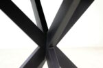 Close-up van kruisende zwarte metalen tafelpoten die een X-vorm vormen tegen een lichte achtergrond.