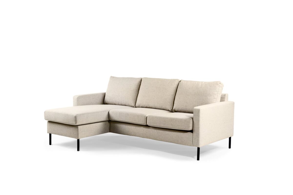 Een beige L-vormige sectionele bank met drie zitkussens en een chaise longue aan de linkerkant. Het heeft zwarte metalen poten en een minimalistisch design tegen een witte achtergrond.