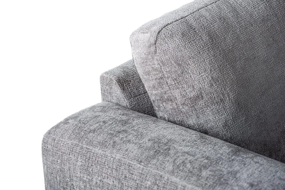 Close-up van een grijze stoffen bank met de armleuning en rugleuning. De structuur van de bekleding is zichtbaar met het weefpatroon van de stof tegen een effen witte achtergrond.