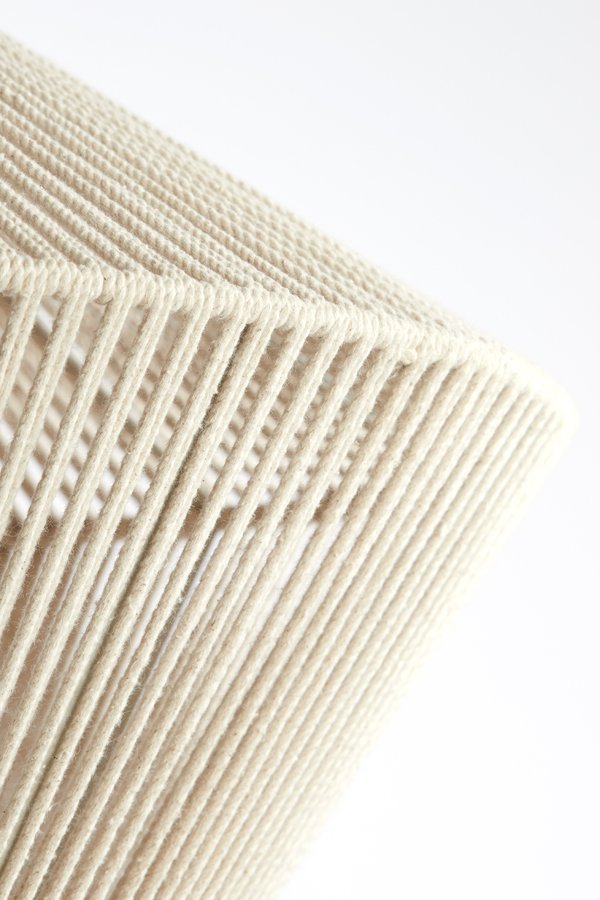 Close-up van de hoek van een geweven, beige lampenkap met snoeren tegen een effen witte achtergrond. De snoeren zijn in een strak, diagonaal patroon gerangschikt, wat een gestructureerde look creëert.