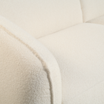 Close-up van een witte, getextureerde stoffen bank. De afbeelding richt zich op de armleuning en rugleuning, waardoor het zachte, pluche materiaal zichtbaar is. De stof lijkt een bouclé-achtige textuur te hebben, waardoor de bank een gezellige en uitnodigende uitstraling krijgt.