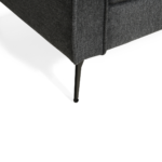 Close-up van een moderne grijze hoekbank met dunne, zwarte metalen poten. De stof lijkt getextureerd en de afbeelding benadrukt het strakke, minimalistische ontwerp. De achtergrond is een effen, helderwit oppervlak, dat de strakke kenmerken van de bank benadrukt.
