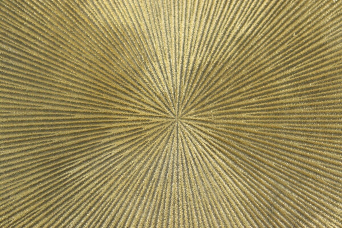 Close-up van een getextureerd, goudkleurig cirkelvormig patroon met stralende lijnen vanuit het midden, wat een stereffect creëert. Het oppervlak heeft een metaalachtige glans, wat het een levendige en lichtgevende uitstraling geeft.