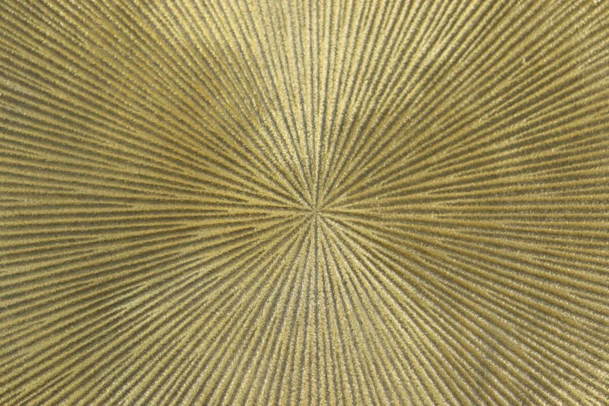 Close-up van een getextureerd, goudkleurig cirkelvormig patroon met stralende lijnen vanuit het midden, wat een stereffect creëert. Het oppervlak heeft een metaalachtige glans, wat het een levendige en lichtgevende uitstraling geeft.