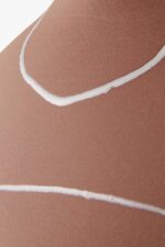 Close-up van de zongebruinde huid van een persoon met witte contouren, mogelijk van het dragen van een badpak. De gladde textuur en contrasterende lijnen suggereren een zonnige dag buiten of op het strand.