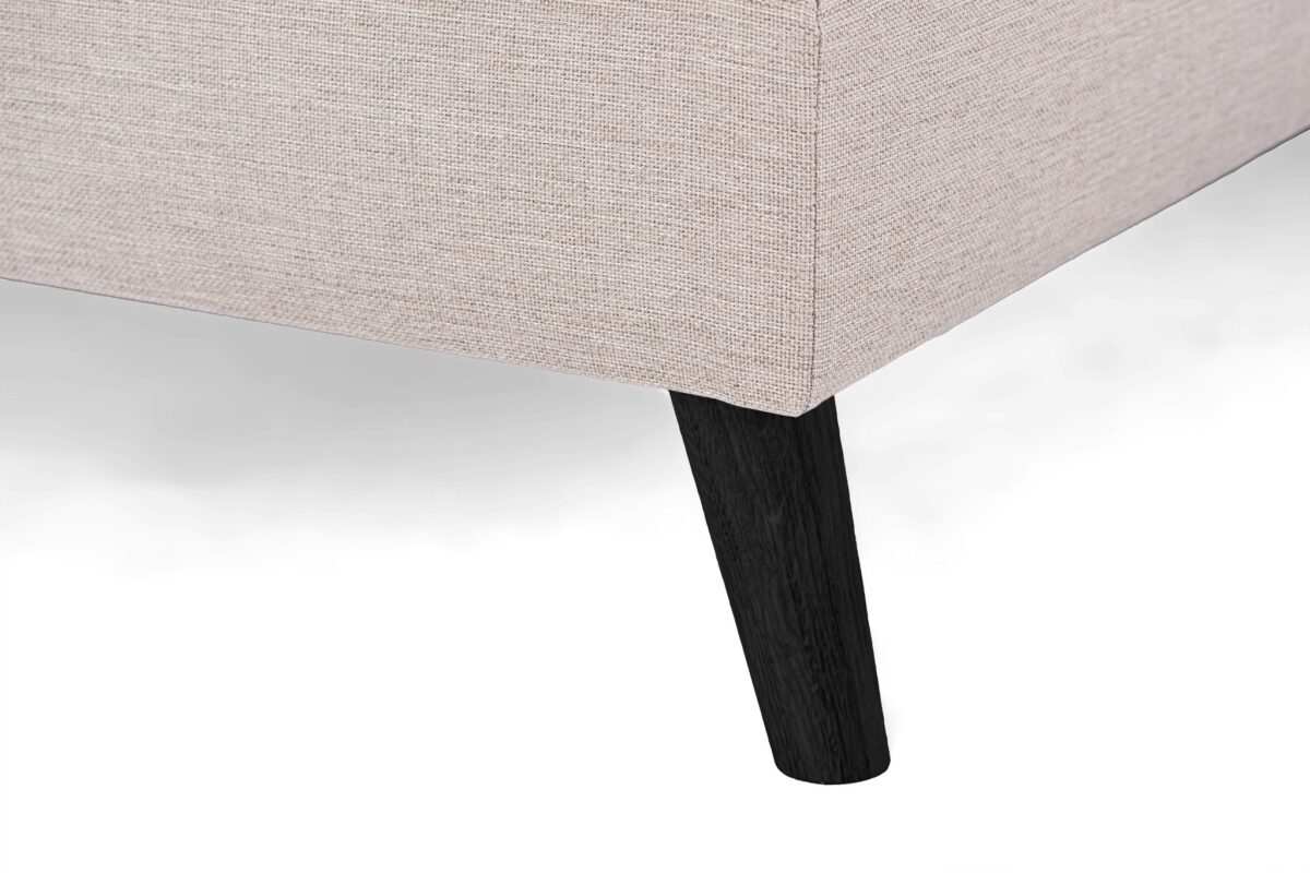 Close-up van een beige, gestructureerde hoek van een bank met één enkele donkere houten poot op een witte achtergrond.