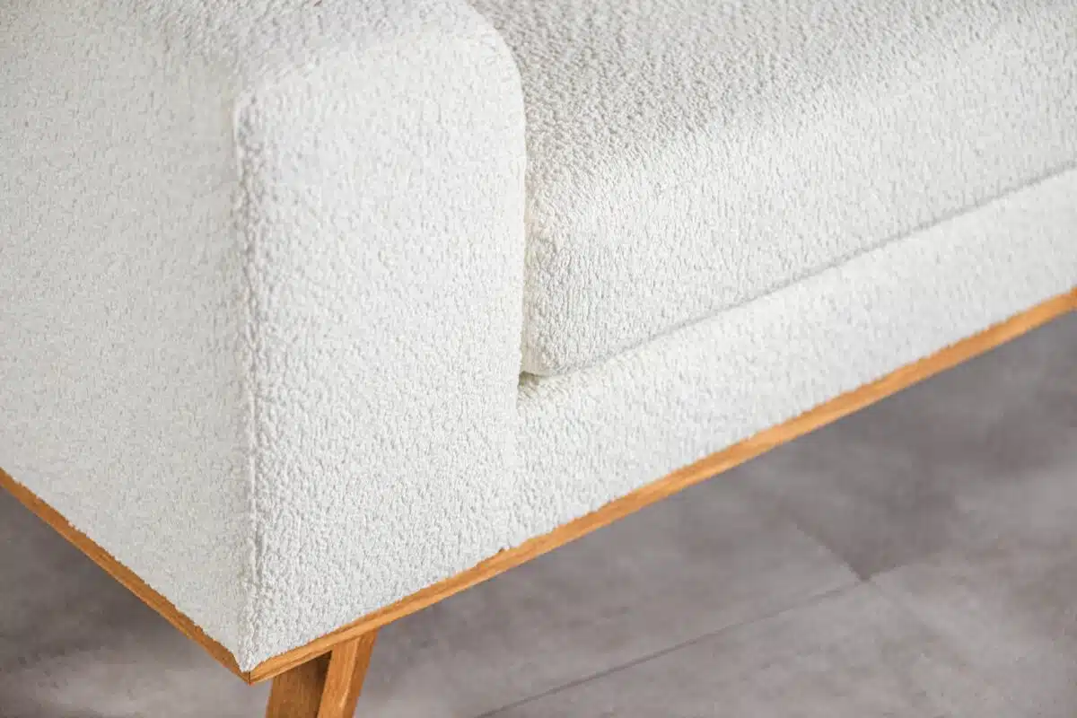 Close-up van een moderne witte stoffen bank met houten poten op een lichtgrijze vloer. Het ontwerp benadrukt strakke lijnen en minimale esthetiek.