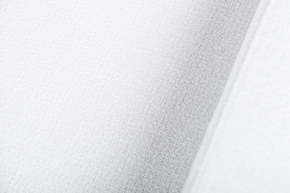 Close-up van een wit getextureerd oppervlak, met fijne, korrelige details. Het oppervlak lijkt licht gebogen met subtiele schaduwen, wat een gevoel van diepte creëert.
