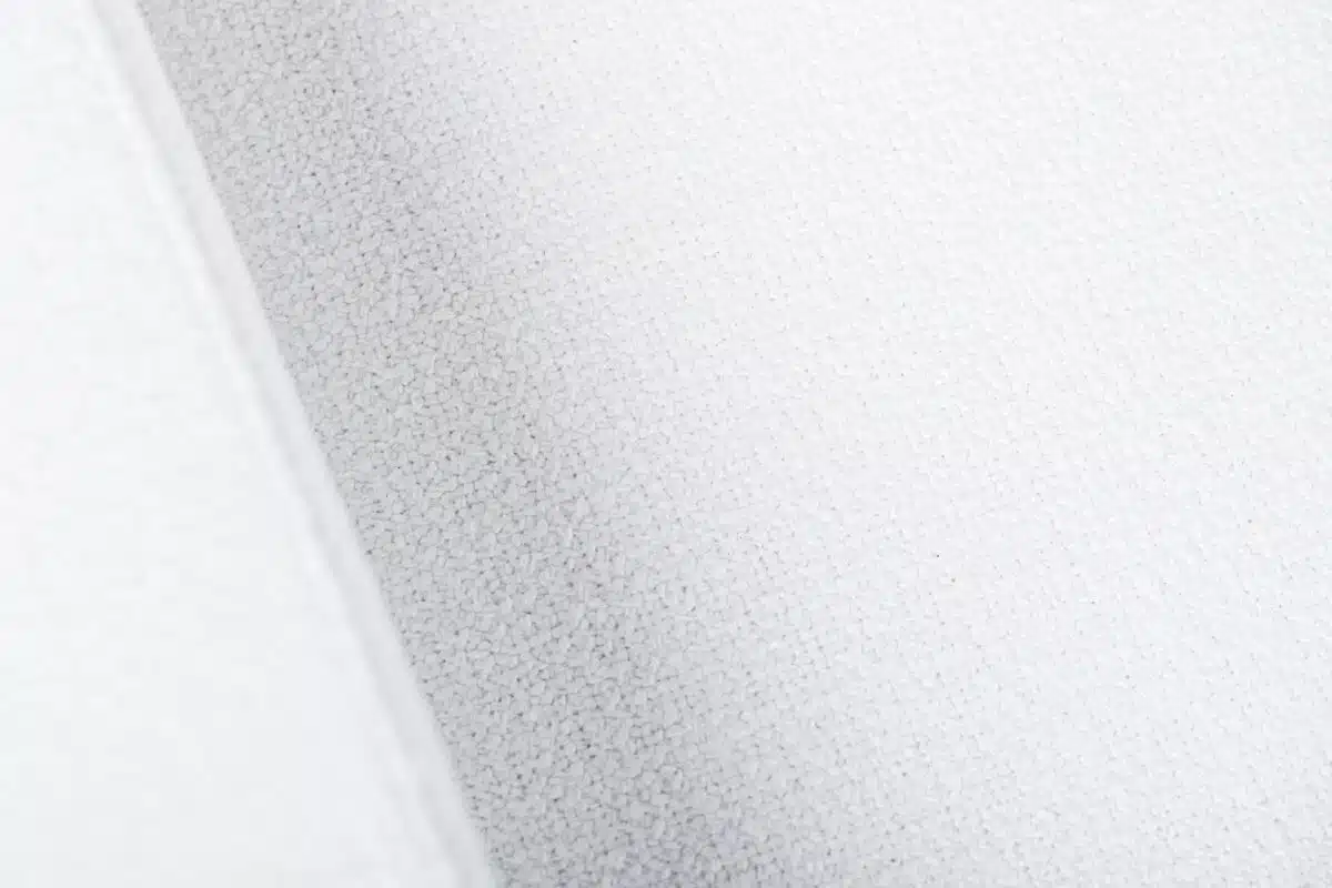 Close-up van een gestructureerd, lichtgrijs oppervlak met subtiele schaduwen. Het oppervlak lijkt stof of papier te zijn, met een fijn, uniform patroon over de afbeelding.