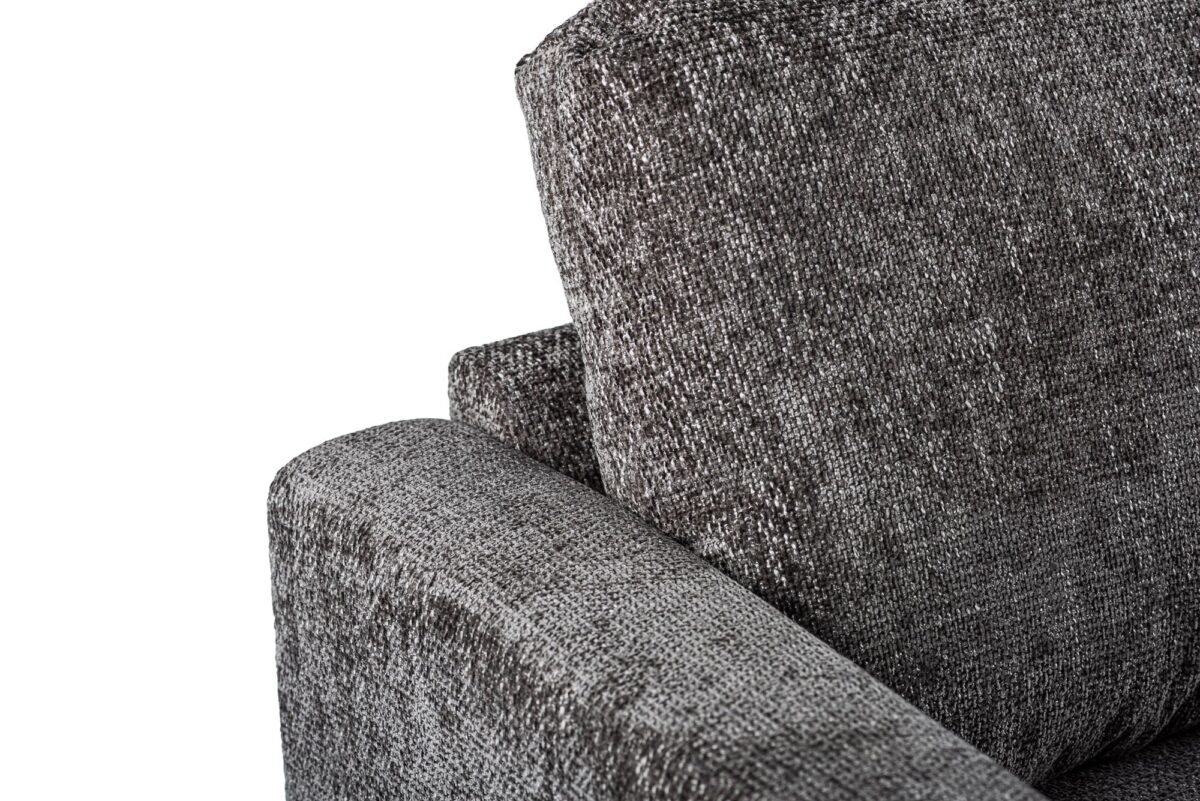 Close-up van een moderne, getextureerde grijze stoffen fauteuil met een focus op de armleuning en rugleuning. De stof heeft een subtiel geweven uiterlijk, wat de stoel een stijlvolle en eigentijdse uitstraling geeft.