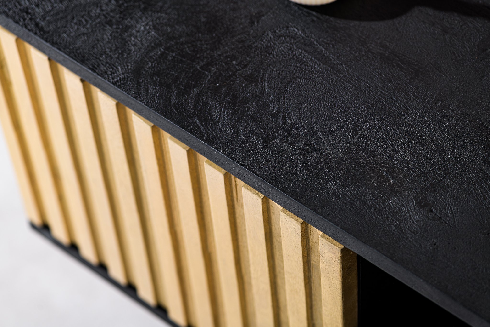 Close-up van een houten tafelhoek met een getextureerd zwart blad en verticale lichte houten latten aan de zijkant. Het minimalistische ontwerp benadrukt het contrast tussen de donkere en lichte houttinten.