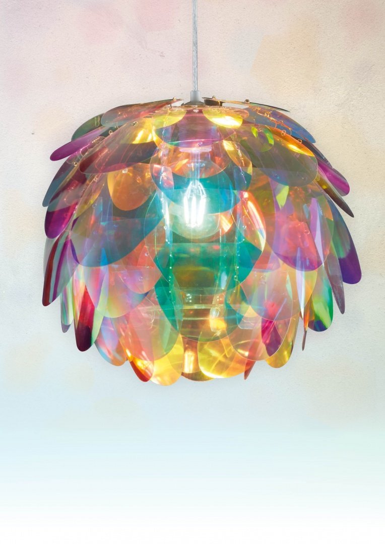 Een kleurrijke, iriserende hanglamp met overlappende bloemblaadjesachtige panelen hangt aan het plafond. De panelen creëren een regenboogeffect en reflecteren licht in verschillende kleuren. Binnenin zit een zichtbare gloeilamp die een warme gloed werpt.