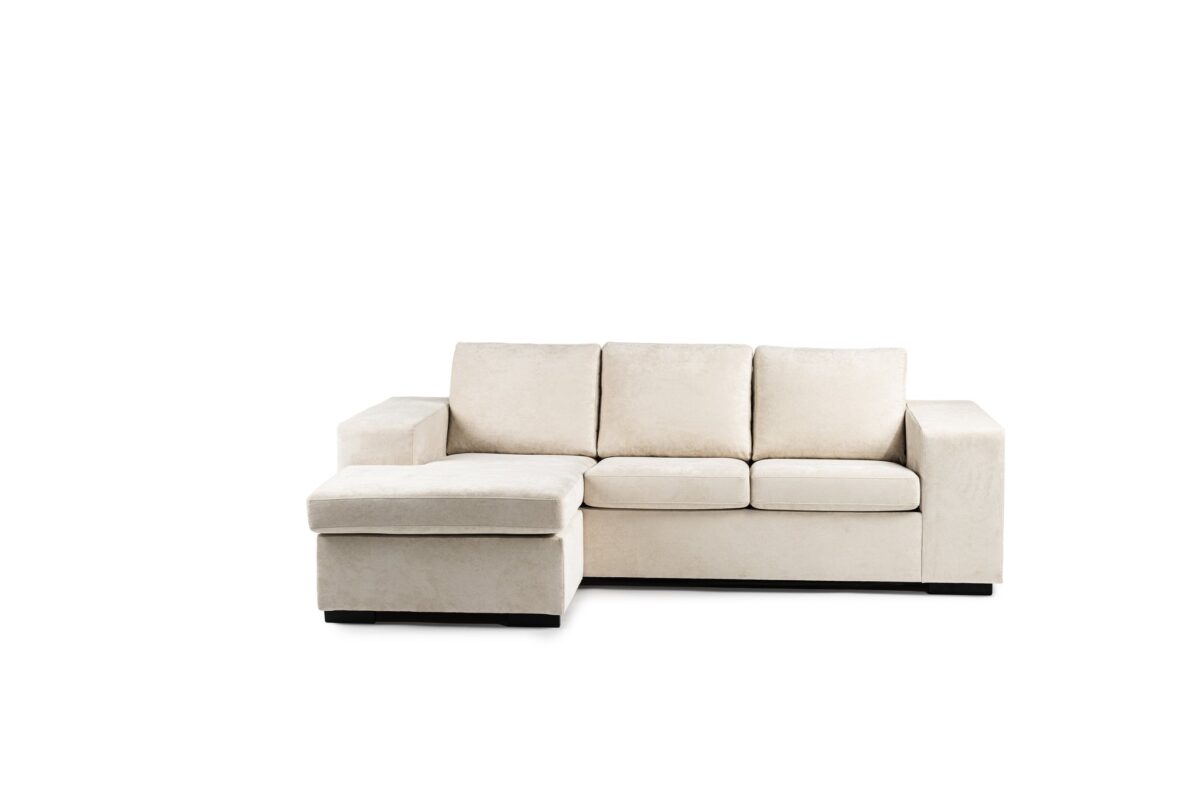 Een crèmekleurige hoekbank met drie zitkussens en een daaraan bevestigde chaise longue aan de linkerkant, tegen een effen witte achtergrond.