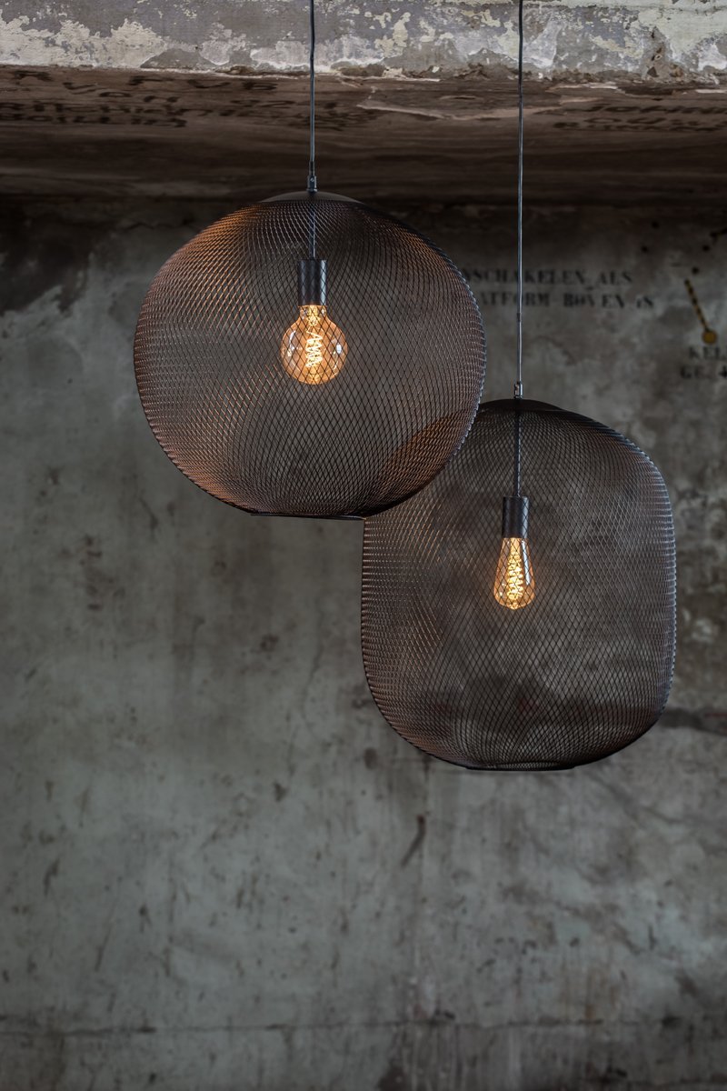 Twee ronde, mesh hanglampen hangen aan een plafond en gloeien warm tegen een getextureerde, industriële betonnen muur. De grotere lamp is iets voor de kleinere geplaatst.