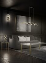 Een moderne woonkamer met een grijze bank en witte kussens. Een eigentijdse spiraalvormige lamp hangt boven een glazen salontafel met gouden poten. Een bijpassende wandlamp en tafellamp zijn ook aanwezig. De kamer heeft donkere muren en een grijs tapijt met textuur.