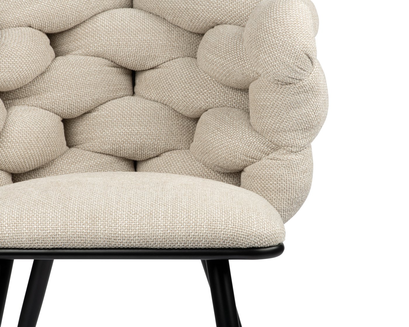 Close-up van een beige, gecapitonneerde stoel met pluche, afgeronde bekleding op de rugleuning en zitting. De stoel heeft een modern design met zwarte poten, met een gestructureerd stoffenpatroon.