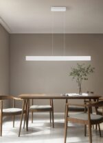 Minimalistische eetkamer met een houten tafel, vier stoelen en een lineaire hanglamp erboven. Een kleine plant in een vaas staat op tafel en de kamer heeft beige muren en een lichte, gepolijste vloer.