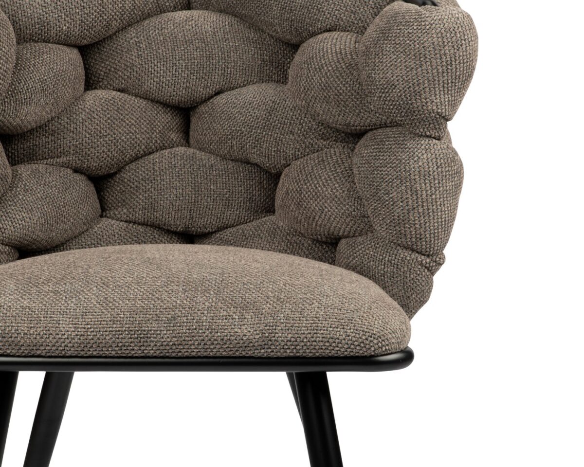 Close-up van een stoel met een getextureerde, geweven stof in grijstinten. Het ontwerp heeft een unieke, gepofte bekleding die lijkt op grote, gewatteerde bubbels. De stoel heeft een zwart metalen frame met slanke poten.