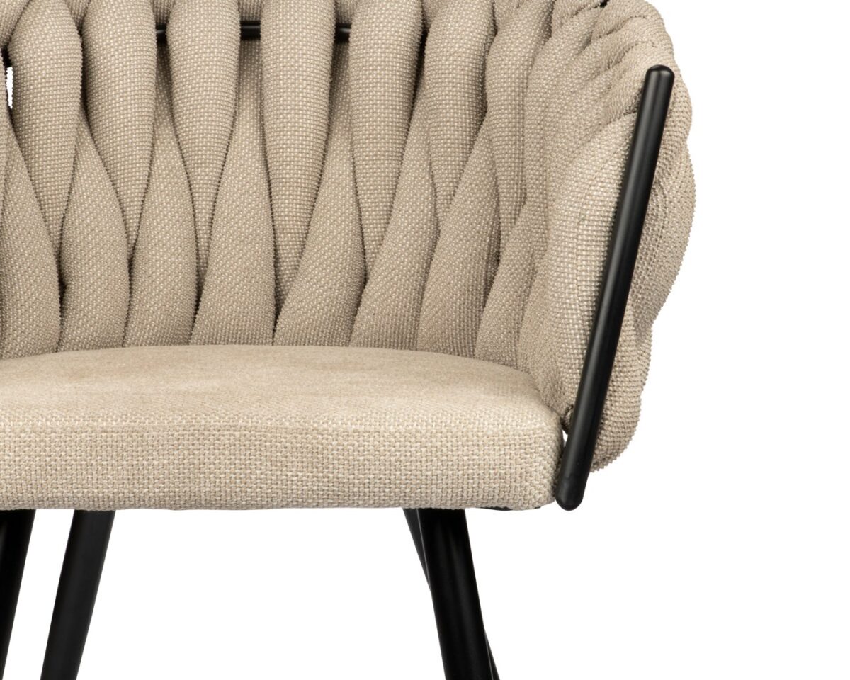 Close-up van een beige geweven stoel met zwarte metalen armleuningen en poten. De stoel heeft een getextureerd, gevlochten rugleuningontwerp en een glad zitkussen. De focus ligt op het bovenste gedeelte, waarbij het ingewikkelde weefsel van de stof zichtbaar is.