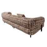 Retro-stijl bruin en wit patroon bank met gebogen randen en mid-century modern design. De stof heeft abstracte vormen en de bank heeft zwarte poten. Van achteren bekeken vanuit een hoek.