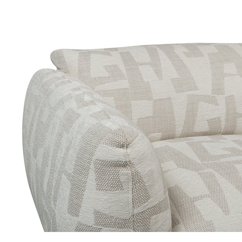 Close-up van een beige gestoffeerde armleuning van een bank met een geometrisch patroon. De stof heeft in elkaar grijpende vormen in een iets donkerdere tint, wat een subtiel contrast creëert. De bank ziet er pluche en comfortabel uit met een modern design.