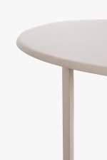Close-up van een minimalistische ronde tafel met een glad, lichtbeige oppervlak en slanke poten, tegen een effen witte achtergrond.