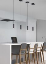 Minimalistische keuken met een wit eiland, vier houten barkrukken met grijze en witte kussens en strakke zwarte hanglampen erboven. Een laptop staat open op het aanrecht bij een moderne kraan en gootsteen. Muren zijn lichtgekleurd.