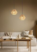 Een gezellige woonkamer met een beige bank, versierd met kussens met patronen en een plaid. Een houten salontafel met een witte vaas en een vaas. Twee geometrische hanglampen hangen erboven en werpen een warme gloed tegen een gedempte groene muur.