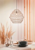 Een gezellige eetopstelling met een geweven hanglamp boven een tafel. De tafel heeft gestapelde donkergrijze borden en heldere glazen flessen. Gedroogd gras en houten lambrisering geven de achtergrond een natuurlijke touch.