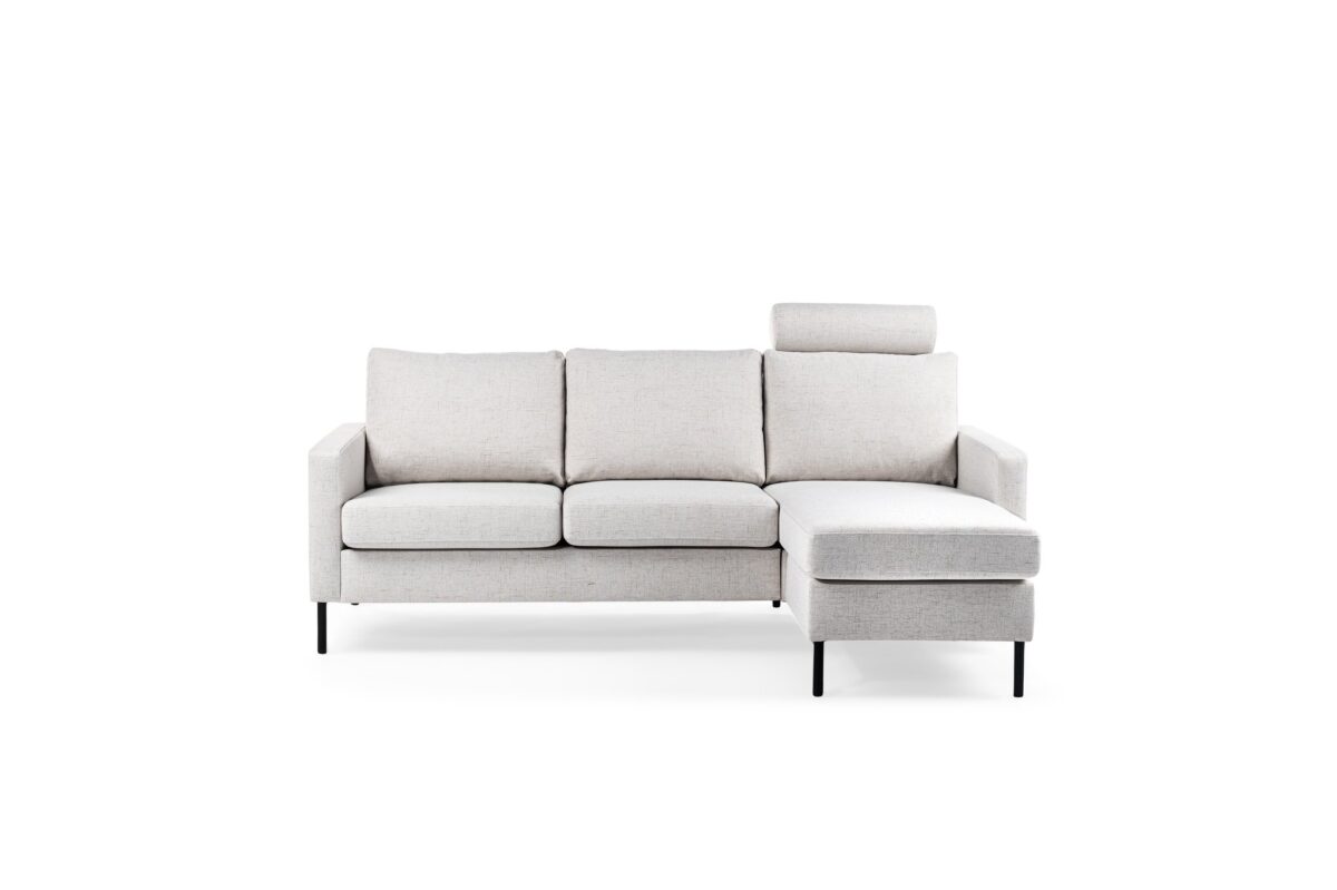 Een moderne, lichtgrijze bank met drie zitkussens en een chaise longue aan de rechterkant. De bank heeft een strak design met metalen poten en een enkele hoofdsteun aan de linkerkant. Hij staat tegen een effen witte achtergrond.