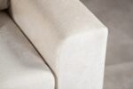 Close-up van een beige armleuning van een bank, met een getextureerde stof. De rand is glad met zachte rondingen en de achtergrond is zacht vervaagd, waardoor de details van de bekleding worden benadrukt.