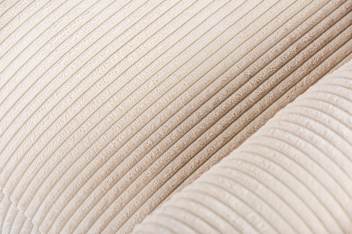 Close-up van een beige corduroystof met verticale ribbels, die de textuur en details laat zien.