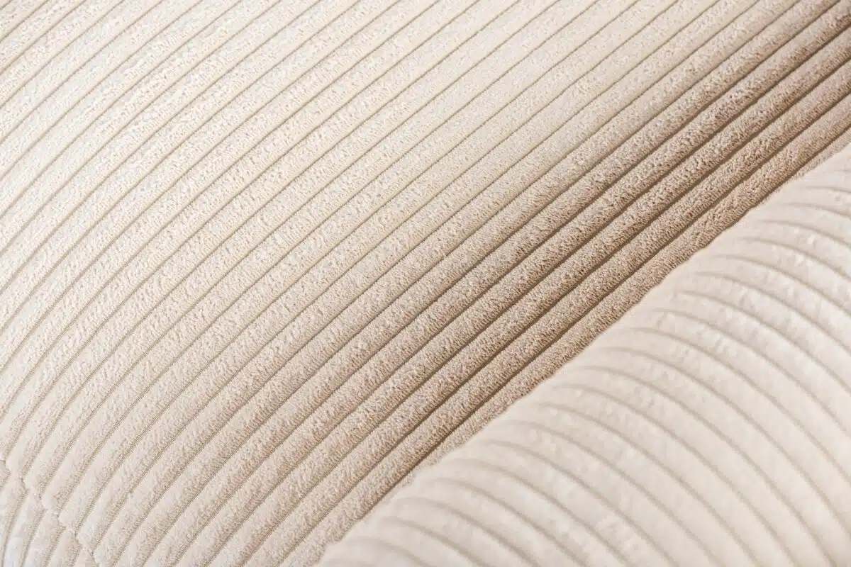 Close-up van een beige corduroystof met verticale ribbels, die de textuur en details laat zien.