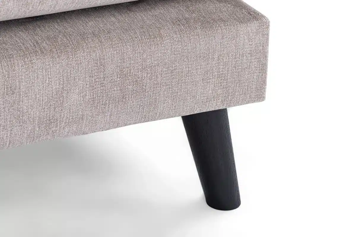 Close-up van een beige gestoffeerde meubelhoek met een donkere houten poot. De stof heeft een gestructureerde uitstraling en het ontwerp is modern en minimalistisch, tegen een witte achtergrond.